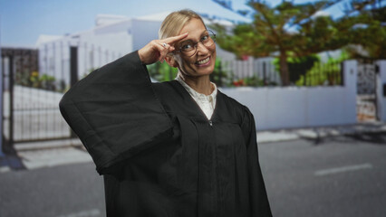 Obraz premium Woman judge in black robe smiles and makes two finger salute on street; confidence celebration warmth.