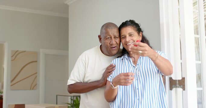 African American couple holding red key fob, showing it at home entry while unpacking boxes