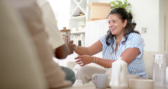 Diverse friends sharing coffee in living room, mature African American woman passing French press