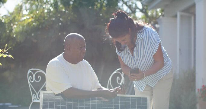 Woman consulting phone while man inspecting solar panel wire and explaining orientation in backyard