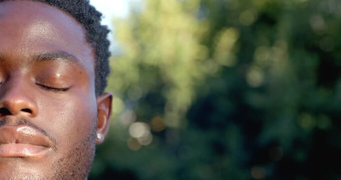 African American man in park, sun causing eyes opening and gaze meeting lens, earring, copy space