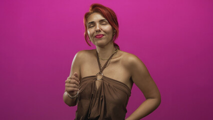 Obraz premium Young hispanic woman with red hair and bare shoulders dancing in pink studio wearing brown halter top and layered necklaces; joy celebration.
