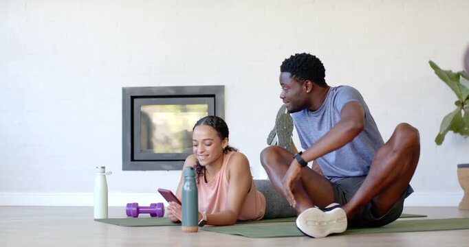 African American couple at home on mats, phone buzzing while woman scrolling and man stretching