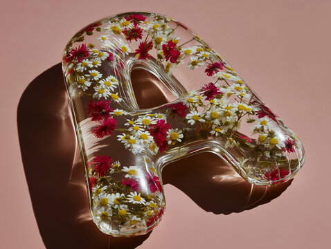 Glass-like letter A filled with wildflowers lies diagonally in dramatic light. Ideal for artistic alphabet graphics, floral packaging, and luxury branding.