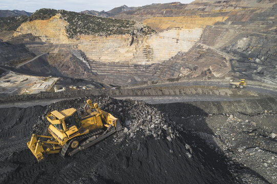 Aerial view of an open-pit mine with a yellow bulldozer working on a pile of ore and terraced excavation walls in Santa Lucia de Gordon, Castile and Leon, Spain.
