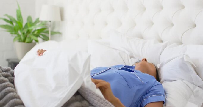 Indian woman waking to morning light, pushing back duvet, rolling and stretching on bed