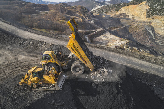 Aerial view of a large yellow dump truck unloading rocks next to a bulldozer in an open-pit mine surrounded by mountains Santa Lucia de Gordon, Castile and Leon, Spain.