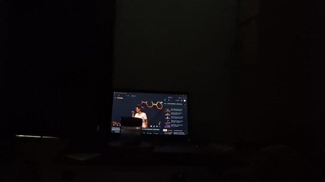 Digital screen in a darkened room showcasing a speaker, capturing the essence of focused engagement with online content, entertainment, or educational broadcasts in a quiet, personal space
