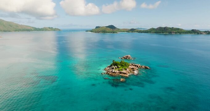A small island surrounded by clear turquoise water with lush vegetation and rocks. St Pierre Island, Seychelles.