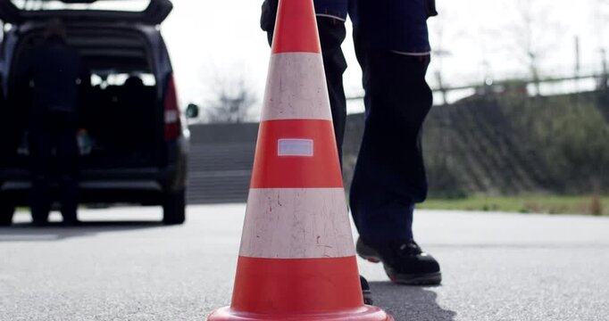 Close up of an orange traffic safety cone with reflective strip on asphalt outdoors and service vehicle