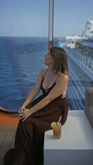 Obraz premium Woman smiling and sitting showing cleavage on cruise ship terrace with ocean view and drink nearby; relaxed serenity.