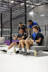 Male teammates reviewing tablet sitting on bench at court in sportswear, holding ball, towel © wavebreak3