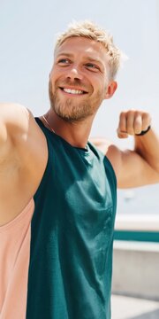 Young man smiling and flexing near waterfront overlook on sunny day