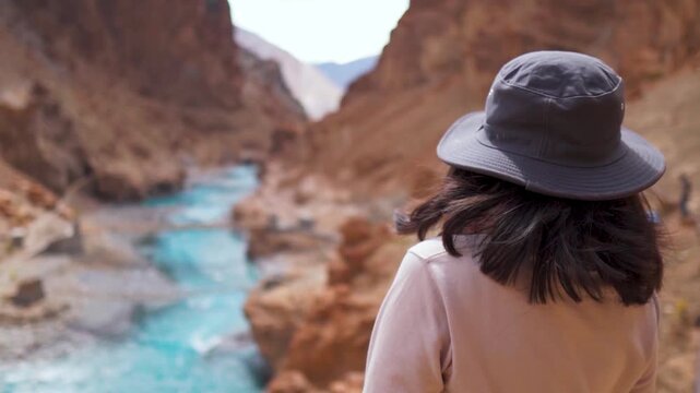 Tourist woman wearing cap looking at mesmerising landscape of Himalaya mountains and flowing Tsarap river during summer season at Zanskar, Ladakh, India. Travel and holidays concept.