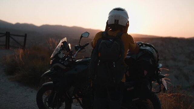 Adventurous motorcyclist taking off his helmet during a sunset break in the desert