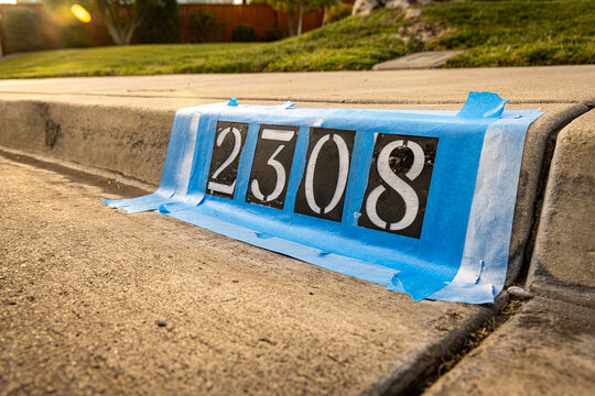 A stencilled address being painted on a sidewalk curb