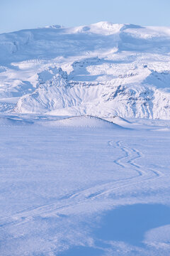 Tyre tracks towards the mountains in a snowy glacial landscape, Iceland