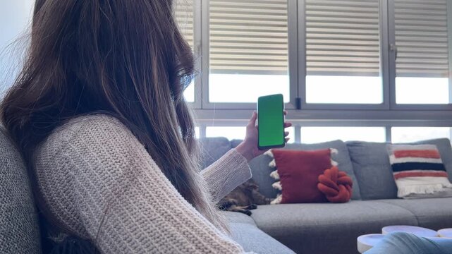 Mujer abriendo persiana con smartphone pantalla verde