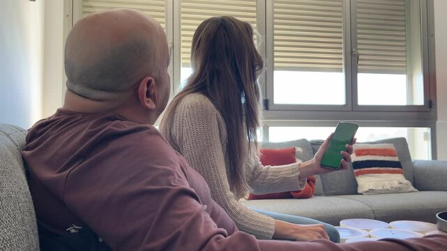 Pareja abriendo persiana con smartphone pantalla verde