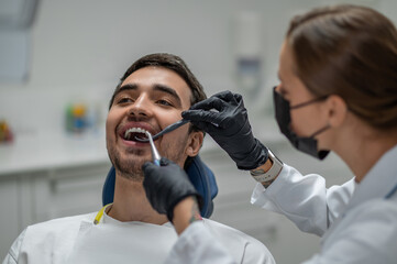 Female doctor in protective mask checking upper jaw of happy male patient with dental tools © zinkevych