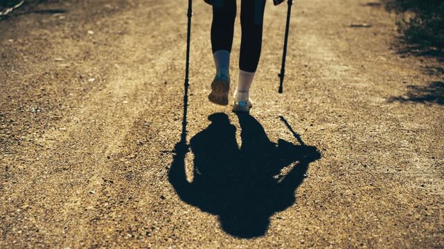 Close-up view of female hiker&rsquo;s legs walking with trekking poles along a mountain trail. Concept of hiking, outdoor adventure, movement and active lifestyle in nature.