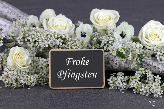 Pfingstgr&uuml;&szlig;e: Stillleben mit wei&szlig;en Rosen und Stiefm&uuml;tterchen auf Treibholz mit Tafel 'Frohe Pfingsten'.&ldquo;