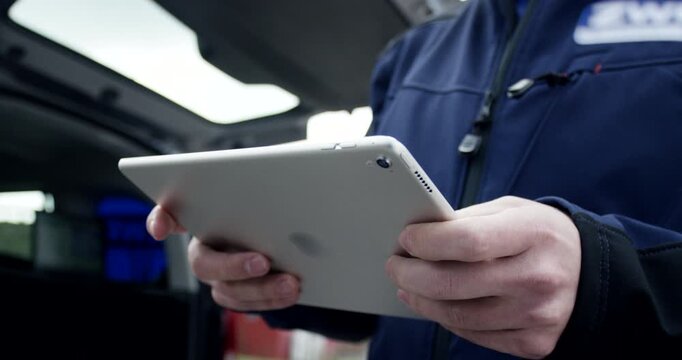 Close up of technician in workwear holding and using digital tablet computer standing by service vehicle