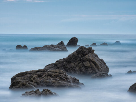 Striking Flysch Rock Leading Line Blue Hour Coast - Dramatic long exposure of a solitary flysch rock formation acting as a leading line towards the mountains under a cool blue hour sky.