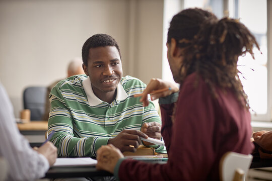 African American teenagers discussing assignment during classroom group work, showing collaboration and peer learning. Useful for education marketing, tutoring, teamwork campaigns
