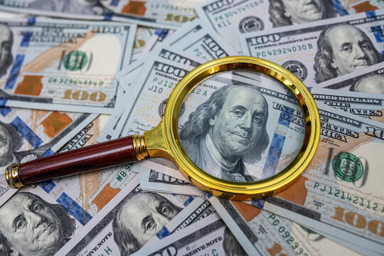 Golden Magnifying Glass on US Dollar Banknotes for Detailed Financial Audit and Tax Inspection