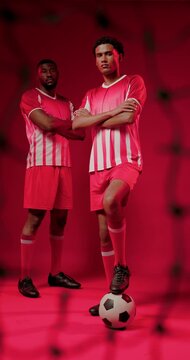 Controlling lead player placing foot on soccer ball in red studio, blurred net and striped jerseys