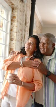 Man is moving behind senior partner, wrapping arms as she is steadying mug, sharing view