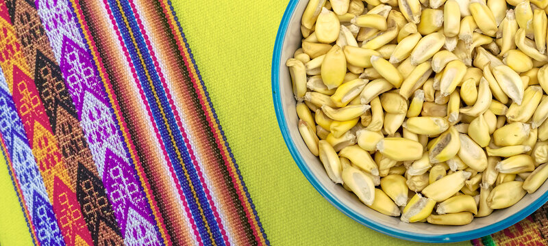  a bowl with a blue-green rim filled to the brim with mote corn kernels on a  Colorful background of traditional peruvian textile fabric, Peru, Latin America