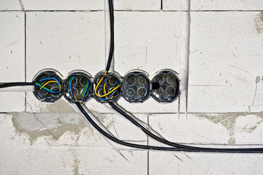 Empty black boxes with cables for electric sockets installed in new house building wall