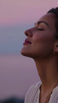 Beautiful woman meditating with her eyes closed, finding peace and tranquility while enjoying the calm moment and breathing fresh air in nature during a beautiful pastel colored sunset