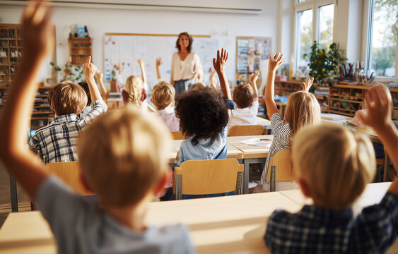 Aula activa con participaci&oacute;n infantil durante explicaci&oacute;n docente. levantan la mano desde sus mesas mientras una persona adulta gu&iacute;a la actividad, transmitiendo inter&eacute;s, dinamismo