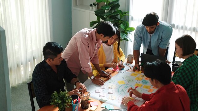 Top view of diverse business people drawing mind map by using marker while brainstorm idea and writing on sticky notes. Group of smart team sharing idea while planning creative strategy. Convocation.