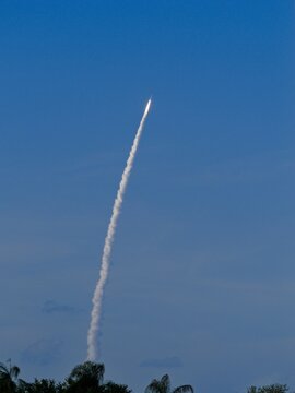 April 1, 2026 Artemis II  rocket launch climbing above tree line with trailing thin bright contrail