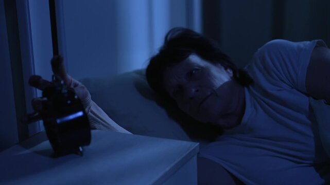 Elderly woman with insomnia tossing and turning looking at clock