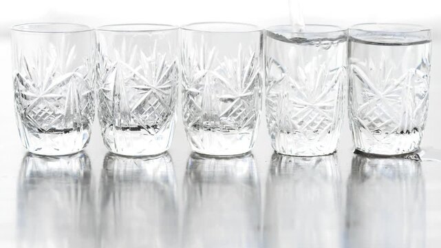 Five transparent glass shots in a row, bartender pouring clear alcohol with pouring sound
