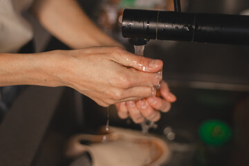 Close up of woman hands carefully washing a brown chicken egg under running water from a black...