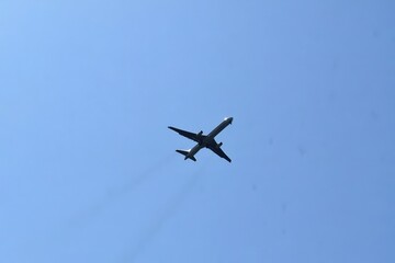 Fototapeta premium A commercial airplane flying high in the clear blue sky, seen from below, during daytime.