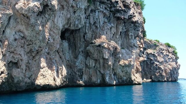 Turkiye, Belek, 27.07.2025 Rocky cliff overlooking blue mediterranean sea in Turkey. Coastal landscape with steep stone walls and calm water surface. Summer travel vacation destination scene.