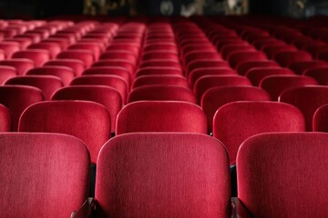 Fototapeta premium Rows of empty red velvet theater seats in a dimly lit auditorium, ready for a performance.