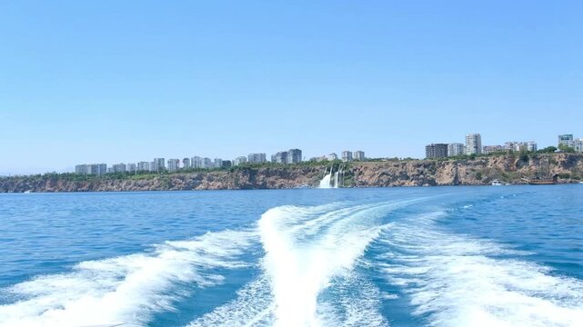 Turkiye, Belek, 27.07.2025 Motorboat wake leaving trail on sea near Turkish coastline. Yacht cruise in Antalya showing cliff and waterfall. Vacation travel concept for coastal excursion.