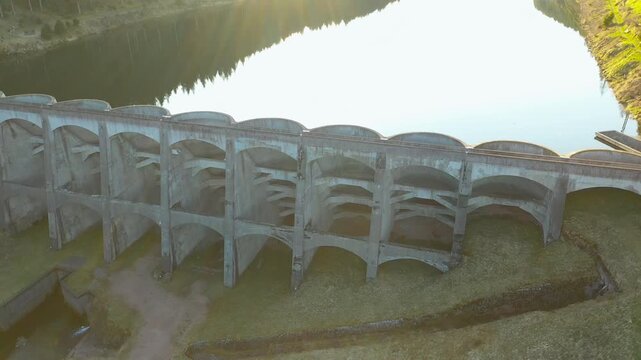Drone side flyby along concrete dam with reflection, cinematic aerial tracking shot