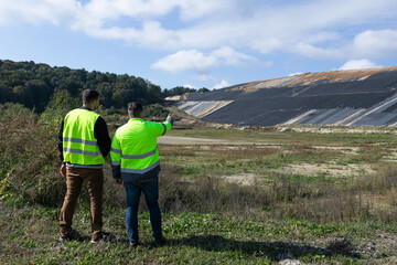 Men in bright vests discuss a landfill area © Orest