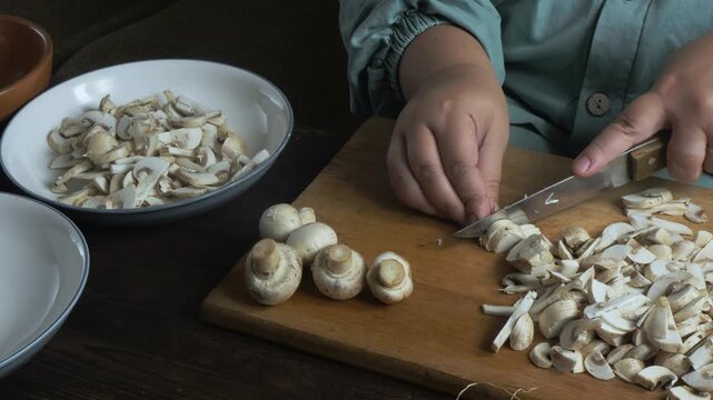 Hands chop fresh champignons with a knife on a cutting board
