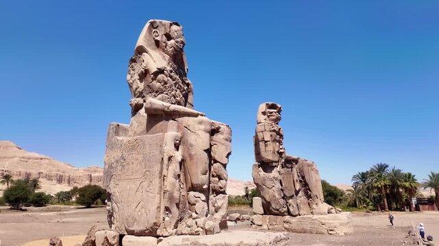 Horizontal zoom out shot revealing tourists visiting the Colossi of Memnon statues in Luxor, Egypt. Travel and cultural tourism editorial concept.