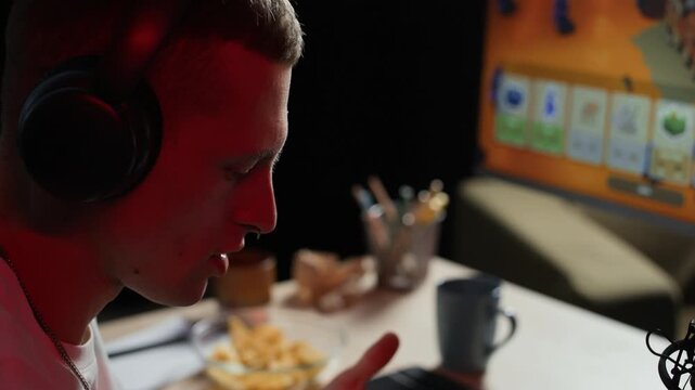 Tilt shot of young Caucasian man reading chat on smartphone and communicating with subscribers while streaming videogame